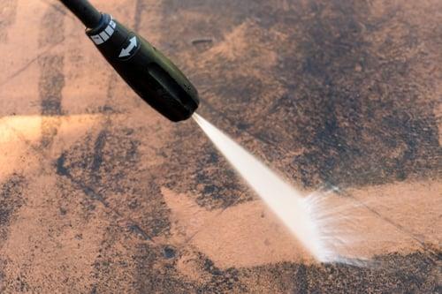Pressure washer cutting a clean line across a dirty paved surface
